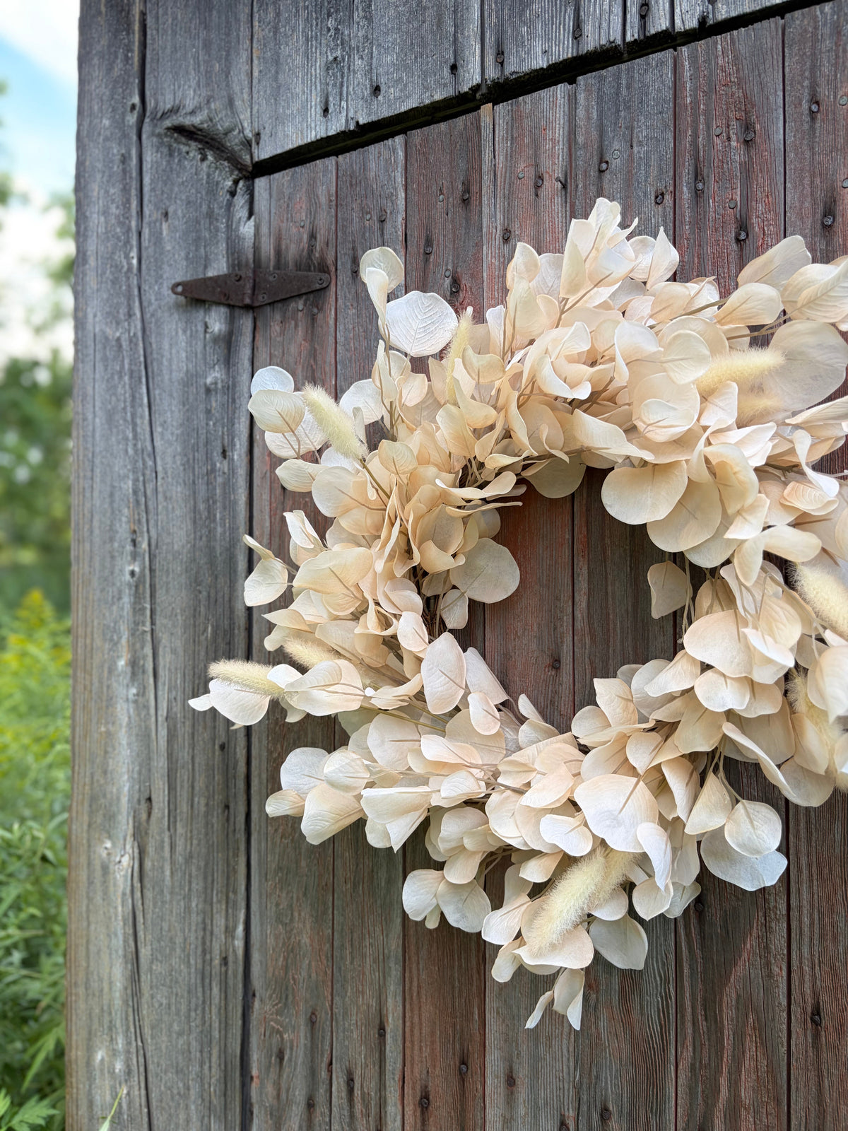 Handcrafted ivory bleached eucalyptus wreath with bunny tail accents hanging on a rustic weathered wood door — neutral farmhouse door wreath